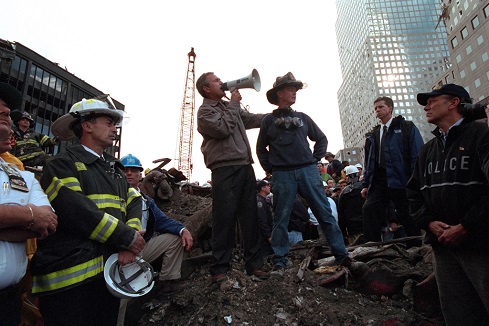 Standing on top of a crumpled fire truck with retired New York City firefighter Bob Beckwith, President George W. Bush rallies firefighters and rescue workers Friday, Sept. 14, 2001, during an impromptu speech at the site of the collapsed World Trade Center towers in New York City. "I can hear you," President Bush said. "The rest of the world hears you. And the people who knocked these buildings down will hear all of us soon."  Photo by Eric Draper, Courtesy of the George W. Bush Presidential Library